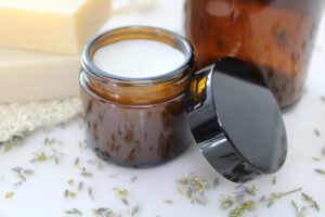 Our Products Delicate natural cream in amber glass jar, surrounded by lavender and beeswax, perfect for skincare routines.