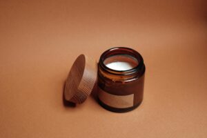Our Products A brown jar with an open lid and candle inside on a brown background, perfect for relaxation themes.