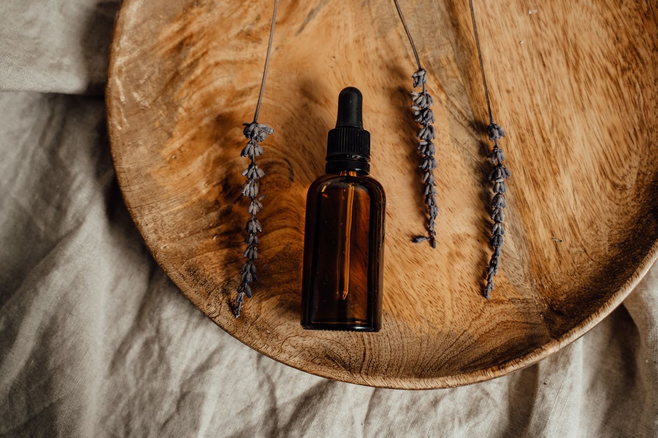 Brown glass dropper bottle with dried lavender on wooden platter, ideal for skincare promotions.